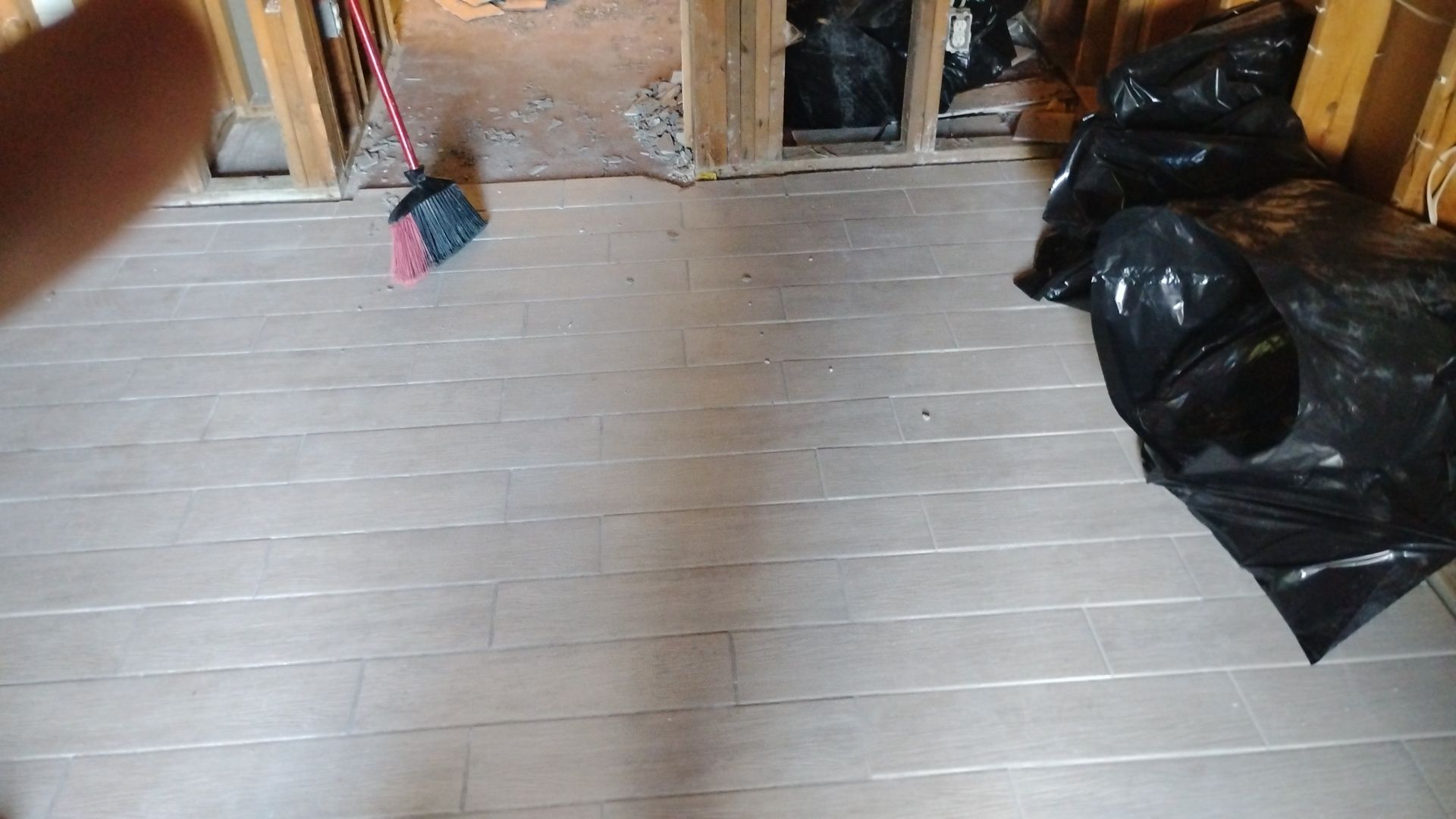 Area after water damage remediation, showing new light-colored tile flooring, exposed wall studs, and a broom for final cleanup.